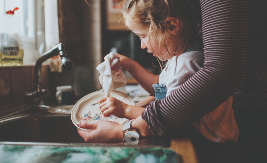 Parent standing behind a child helping them to wash a plate