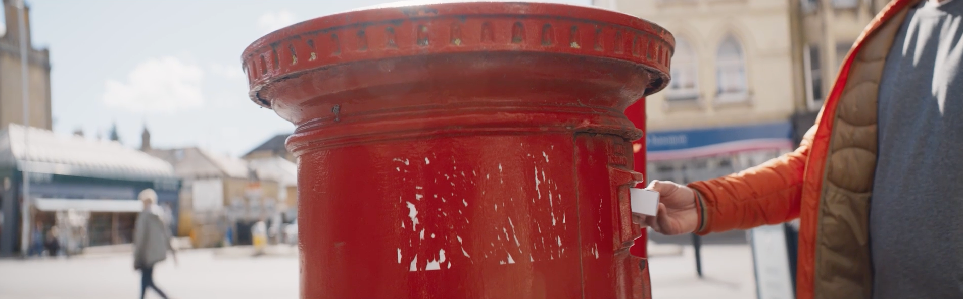 A person placing a white box into a red post box.