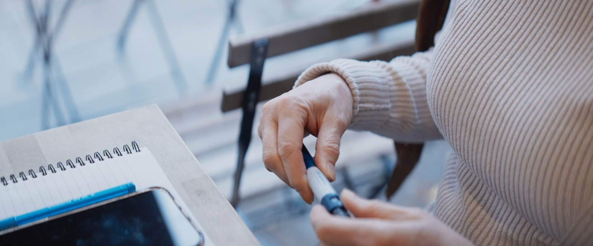Close-up of hands handling a Novo Nordisk pen device, with a notepad and smartphone visible on the table beside them.
