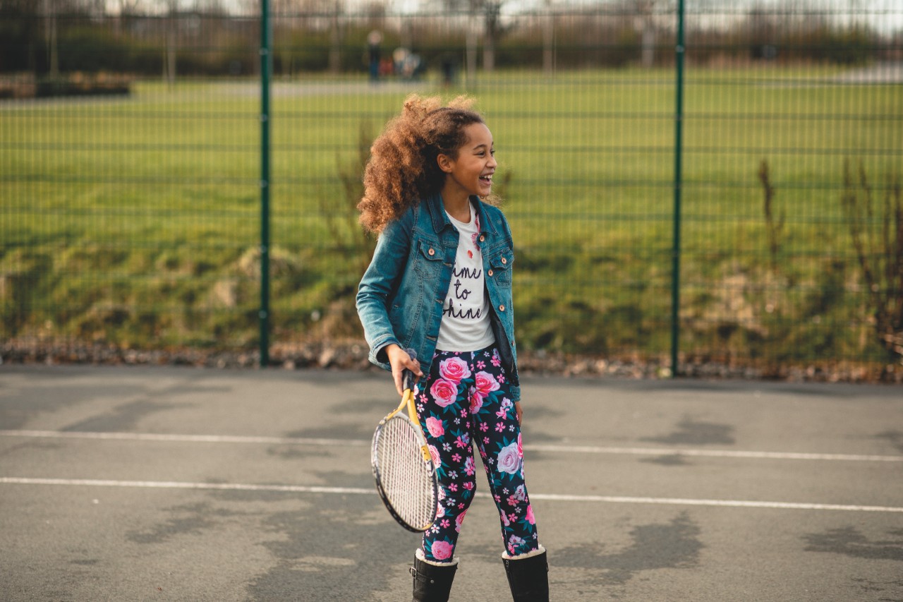 Girl smiling as she looks away, tennis racket in hand as she stands in the sport court.